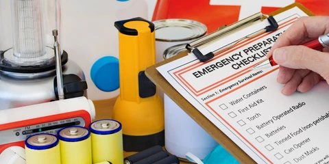 Emergency supplies checklist on a clipboard, surrounded by emergency supplies like batteries, flashlight, and canned goods