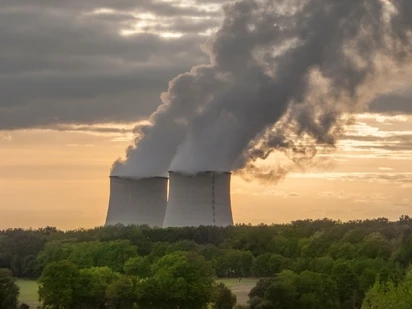 Nuclear Power plant with smoke rising into the sky surrounded by trees