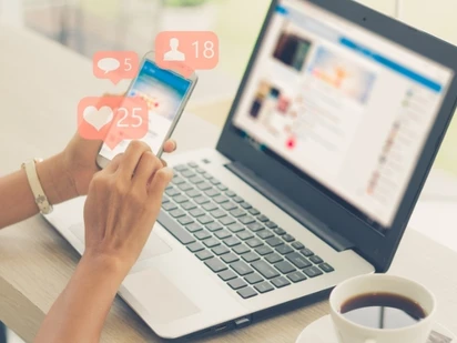 Woman checks social media reactions on phone and laptop. 