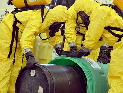 Workers in HazMat suits handle toxic chemicals in barrels