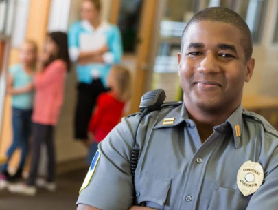 Security guard poses with school children and teacher in the background.