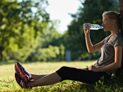 Woman drinking water in shade of tree.