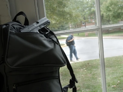 Backpack with gun sits by window with man walking outside window in background..