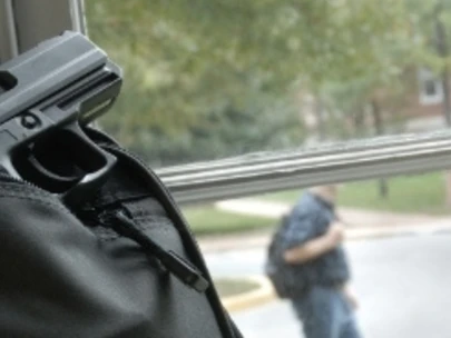 Backpack with gun sits by window with man walking outside window in background..
