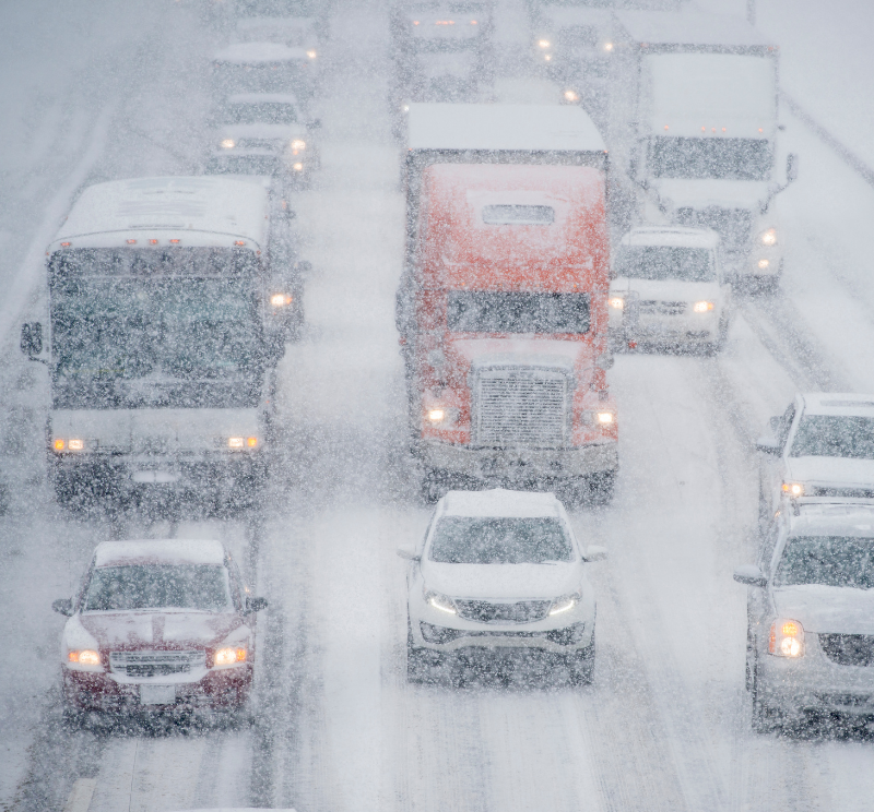 Buses, semi trucks, and cars drive down a busy interstate during a winter storm