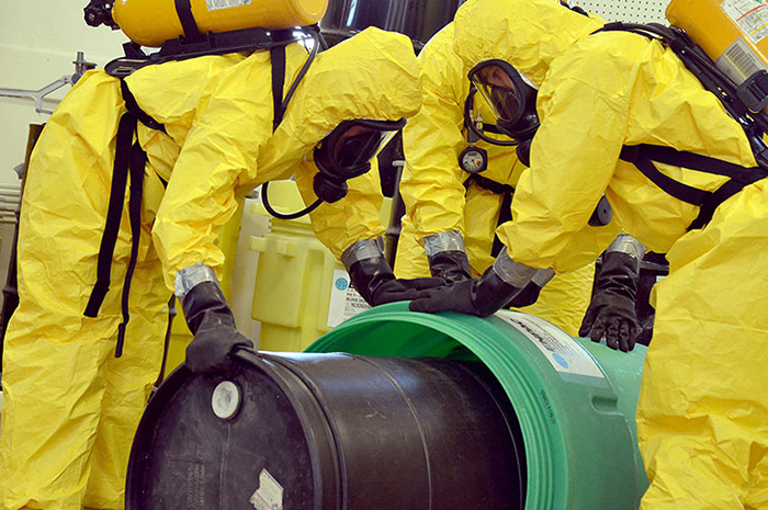 Workers in HazMat suits handle toxic chemicals in barrels