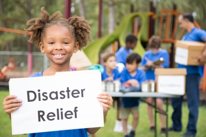 Child holds Disaster Relief sign while others take donations